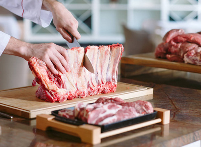 男厨师的手在餐馆里用刀切生排骨照片