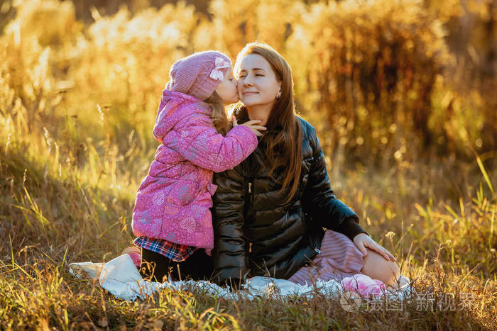 他们坐在草地上的毯子上,女儿亲吻她的母亲,母亲微笑. 肖像画