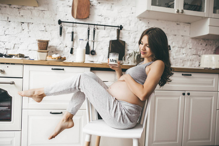 美丽的怀孕妇女在厨房与牛奶杯