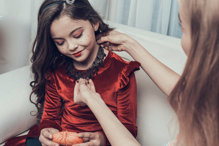 漂亮的女人把黑色项链戴在小女孩身上。 美丽的母亲帮助可爱的微笑女儿参加万圣节派对。 庆祝万圣节。 家庭和儿童概念