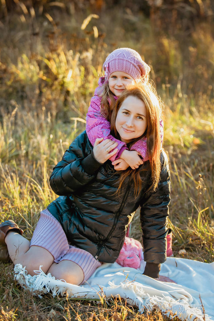 年轻漂亮的母亲和她的女儿在阳光明媚的秋天散步.