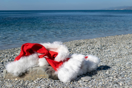 圣诞老人的衣服和帽子躺在海滨的一块大石头上