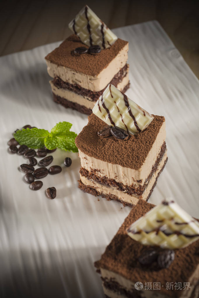 三个方形的提拉米苏蛋糕,上面装饰着微型白条巧克力