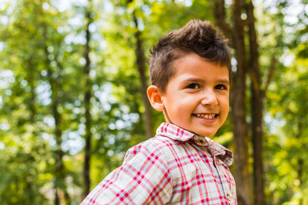 一个微笑的男孩在秋天的树木背景上的肖像。