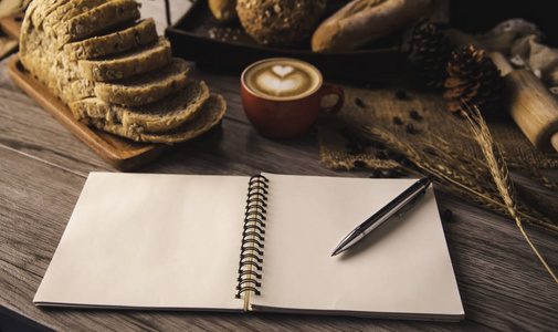 笔放在铺在桌子上的白色笔记本上，放着咖啡和面包。