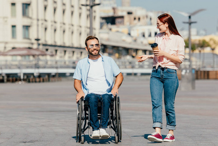 微笑着坐轮椅的英俊男友和喝咖啡的女朋友上街散步