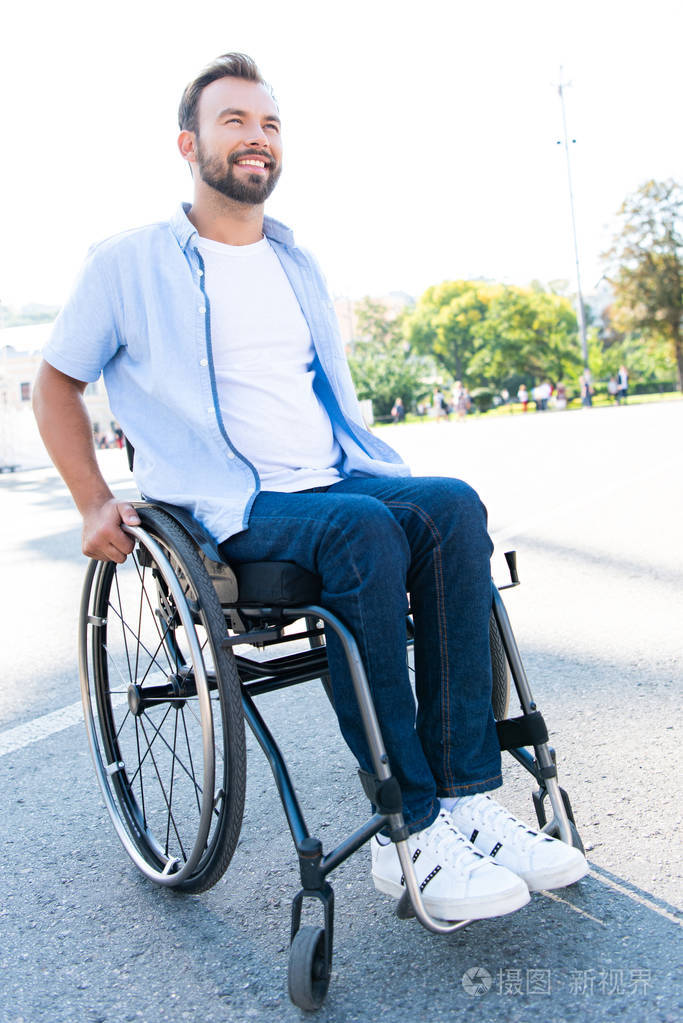 英俊的微笑男子坐轮椅在街上抬头仰望