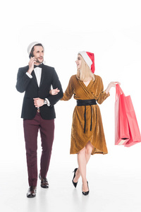 有魅力的男人在智能手机上说话，女朋友在圣诞老人帽子上，购物袋被隔离在白色上