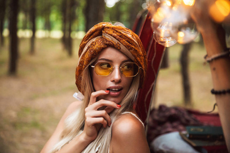 夏天嬉皮士女人穿着时尚配饰在森林营地休息时向前看的照片