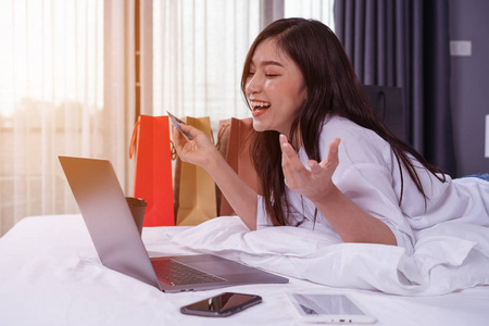 幸福的女人用笔记本电脑上网购物，床上有信用卡