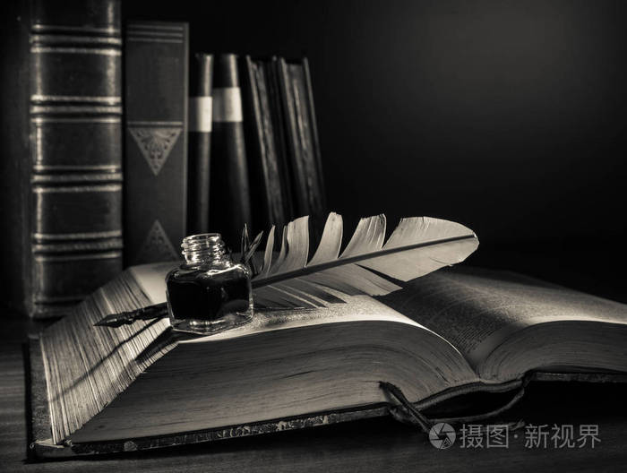 羽毛笔和一本打开的书放在木桌上,旧书有黑白效果