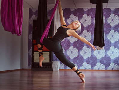 在健身俱乐部的紫色吊床做空中瑜伽练习的年轻妇女