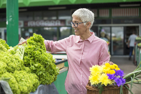 老妇人的画像拿着花篮，在市场上买生菜