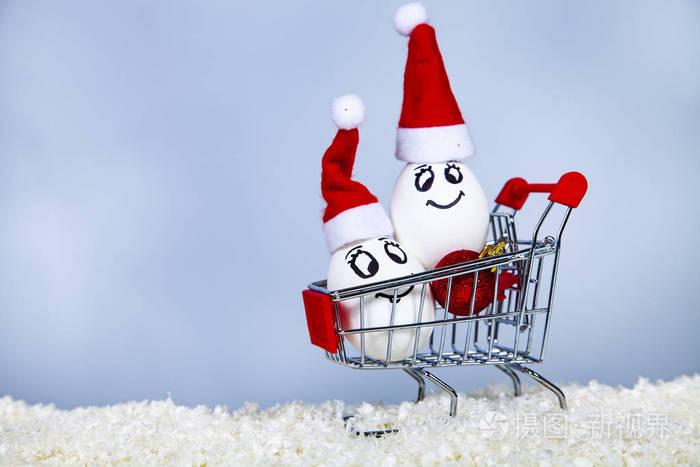 两个鸡蛋在圣诞帽上放在雪上的购物车上。 圣诞节购物。 圣诞义卖。