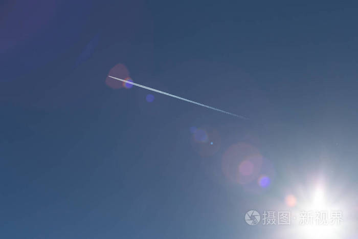 在德国南部6月阳光明媚的一天，你可以看到蓝色的夏日天空上有白色的小径和透镜光学效果的喷气式飞机。