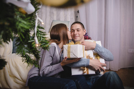 一对年轻夫妇带着礼物在新年树附近，房间里装饰着玛丽圣诞节和新年