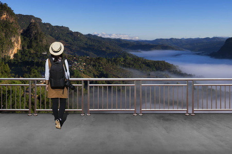 亚洲女游客穿着休闲服装,带着简单的背包和照相机,看着秋天的风景照片