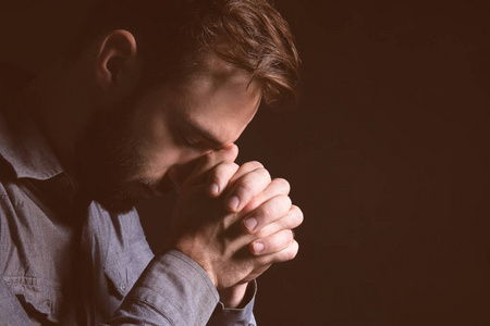 宗教青年向黑背景的上帝祈祷