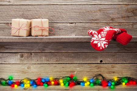 圣诞灯礼品盒和手套在木墙前。 为你的问候留出空间