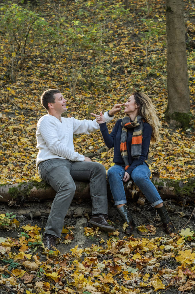 年轻快乐的情侣坐在秋天坐在秋天森林里一棵倒下的树上在黄色的落叶中