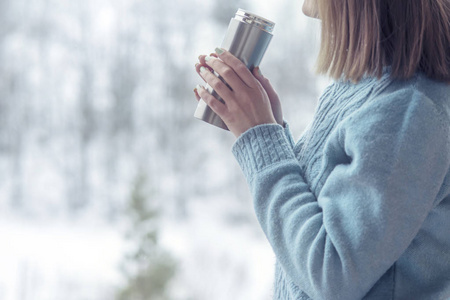 女人在冬天森林的背景下，手里拿着热水瓶