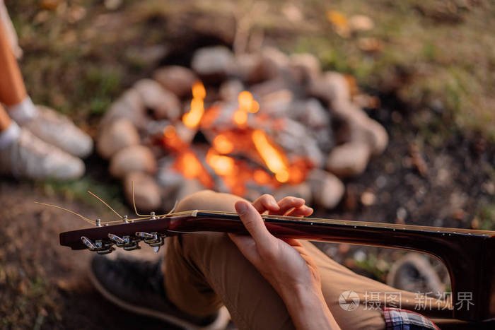 特写年轻人玩吉他附近篝火在日落远足