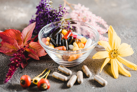 玻璃碗中的药理丸和木制桌面上的彩色花的替代药物概念