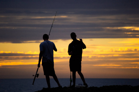 日落时两个人在海滩上钓鱼的剪影