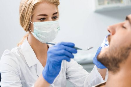 年轻的女牙医检查英俊的微笑客户的牙齿