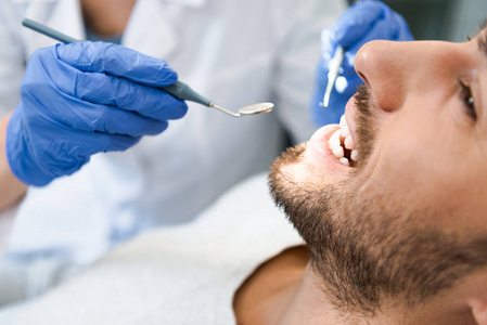 一张剪下来的牙科医生检查英俊的微笑客户的牙齿