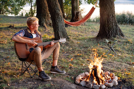 年轻人玩吉他附近篝火露营在远足照片