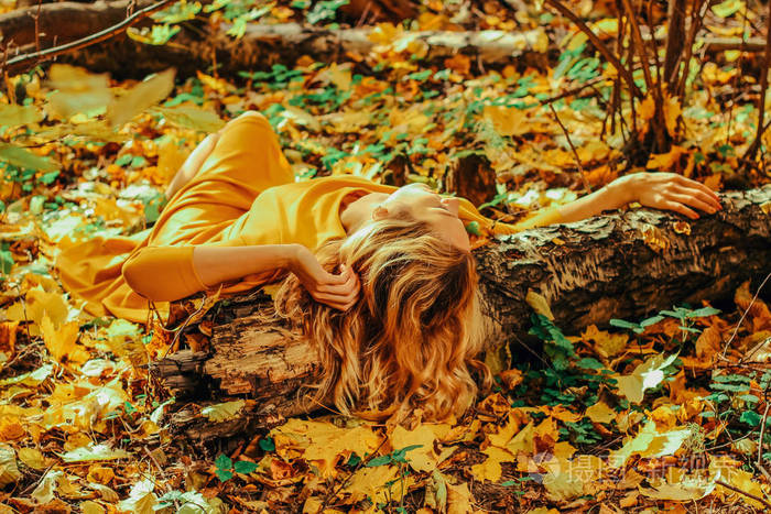 年轻美丽的女孩在一个长黄色的礼服躺在秋天的落叶公园的地面上, 黄叶