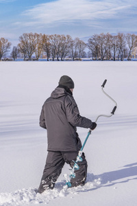 冬季捕鱼的概念。 渔夫在行动中，手里拿着冰螺钉在湖面上做着雪冰