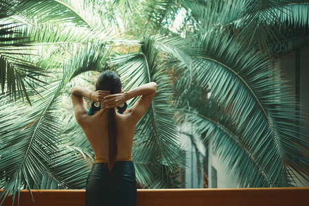 安排她的头发后景适合异国情调的女人裸背,看着巨大的棕榈树叶,而休息