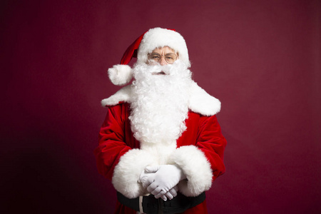 圣诞老人的肖像，穿着圣诞老人的服装，看着摄像机，在红色背景上摆姿势，圣诞节和新年的概念