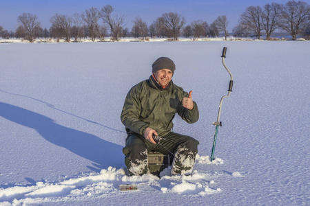 冬季捕鱼的概念。 渔夫在行动。 从雪冰上抓鱼。