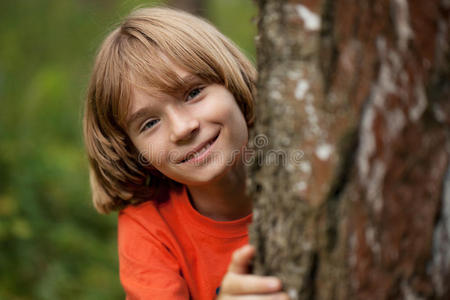 穿着红色T恤的男孩从树干后面偷看