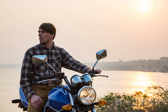 年轻的男性旅行者骑摩托车迎接美丽的日落