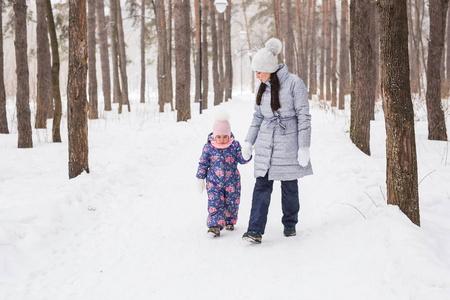 家庭, 冬天和自然概念年轻开朗的母亲与可爱的小女儿走在雪地公园