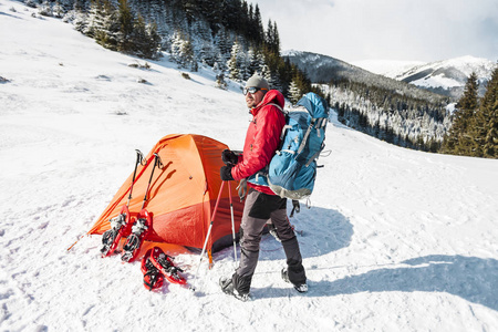 在雪地里露营。 冬天在山上徒步旅行。 橙色帐篷雪鞋和徒步旅行杆。 一个带背包的人在雪地上搭帐篷。 极端的旅程。 冬季徒步旅行的设