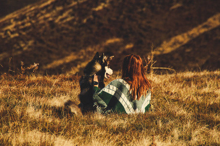 一个女孩穿着一件真正的斗篷，带着绿色图案玩哈士奇。 秋天的乌克兰喀尔巴阡山脉。 温暖的彩色绿叶。森林和山脉的顶部景色。 狗的旅行