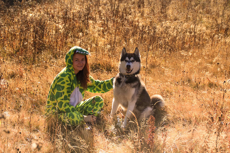 西伯利亚哈士奇和红头发的女孩穿着龙服，在乌克兰喀尔巴阡山脉的田野里迎接日出。 一只黑白相间的狗在和一个女人玩。 可爱的哈士奇。