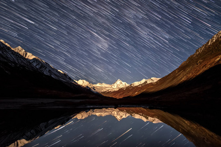令人惊叹的夜景，星光以足迹的形式出现在雪山的山峰上，月光和湖中的倒影为背光