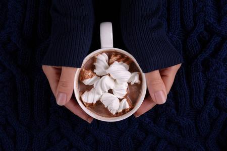 女人的手拿着热巧克力和棉花糖糖在蓝色针织格子。 上面的风景。 复制空间