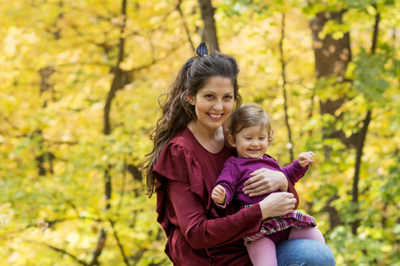快乐的母亲在秋天的公园里拥抱她的女婴。母亲和女儿。幸福的家庭母亲和小孩子在大自然中。