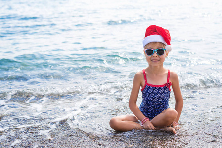 可爱的女孩在海滩上庆祝新年和圣诞节，戴着圣诞老人免费空间的帽子。 热带国家的圣诞节背景寒假。