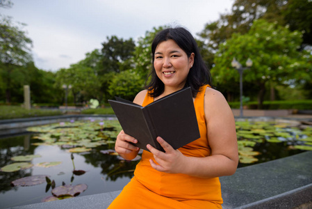 快乐超重亚洲妇女阅读书在公园