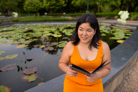 美丽的超重亚洲妇女微笑和阅读书在公园