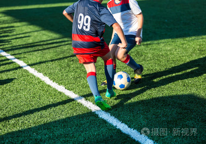足球队的男孩穿着红色蓝色白色运动服在绿色的球场上踢足球. 孩子们运