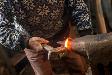 老铁匠用锤子在铁砧上手工锻造熔融金属。
